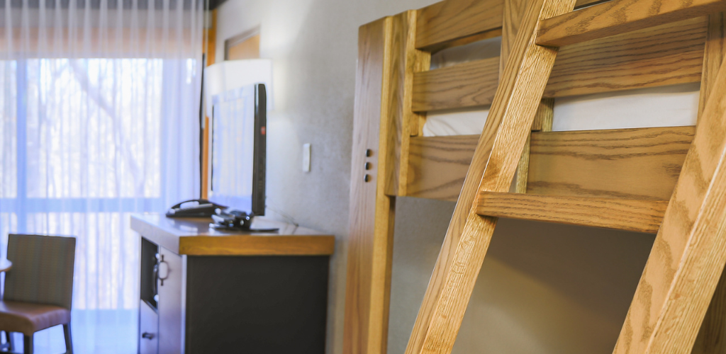 A guest room at Shawnee Lodge with a close up of a corner of a bunkbed. In the background is a queen bed and TV on top of a chest of drawers.