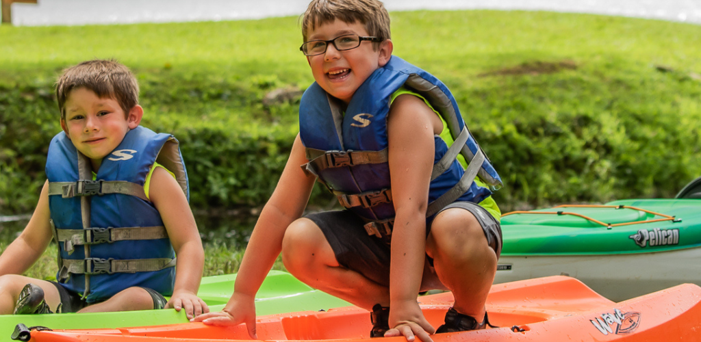 Two young boys sitting in kayaks on land